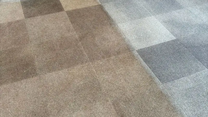 A blue commercial carpet tiled floor in a club house. The uncleaned left side shows a dirty brown floor and the right side shows a blue carpet following a deep clean.