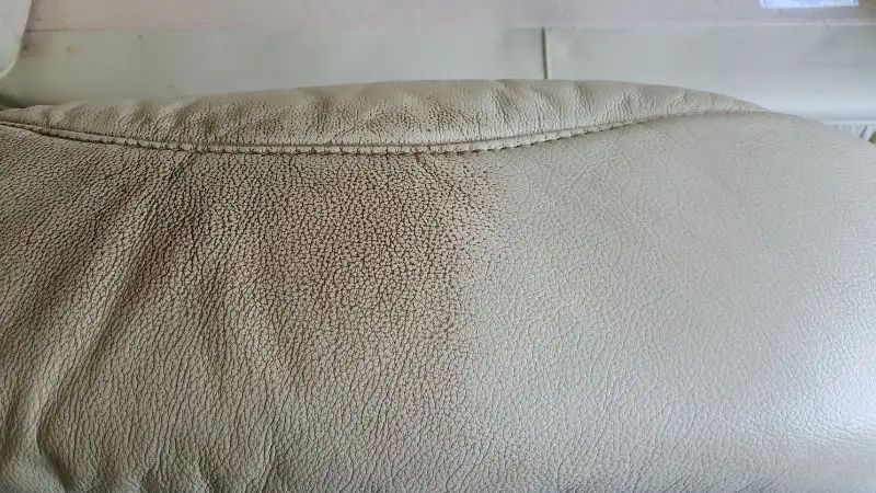 A close-up image of a cushion of a leather armchair. This is a cream coloured cushion that is very dirty on the left side. The right side has been cleaned and shows the restored colour.