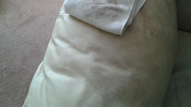 An arm of a leather sofa with a dirty cloth on top. The left side of the arm is clean and the right side is still dirty. The cloth shows the dirt that has been removed so far.